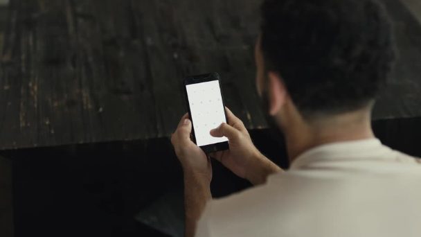 Over the shoulder of a man on his phone at a dark table